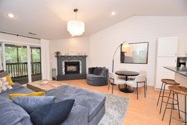 living room with vaulted ceiling, wooden walls, a tile fireplace, a notable chandelier, and light hardwood / wood-style floors