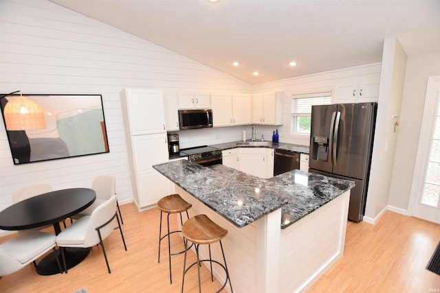 kitchen with a kitchen island, light hardwood / wood-style flooring, dark stone countertops, white cabinets, and appliances with stainless steel finishes