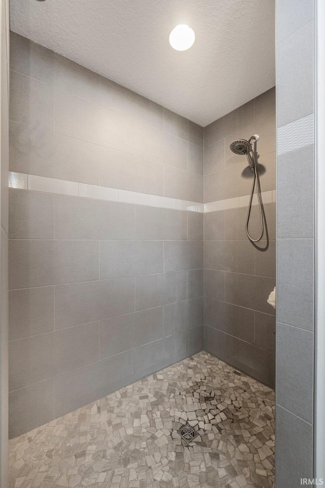 bathroom with a textured ceiling and tiled shower