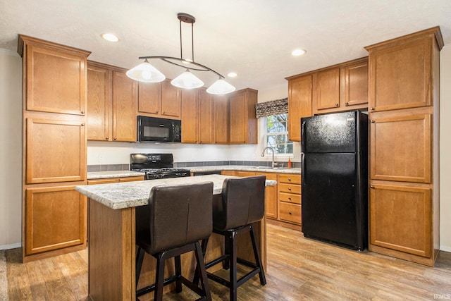 kitchen featuring black appliances, sink, hanging light fixtures, light hardwood / wood-style floors, and a kitchen island