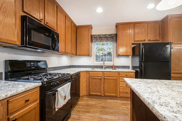 kitchen featuring light stone counters, sink, black appliances, and light wood-type flooring