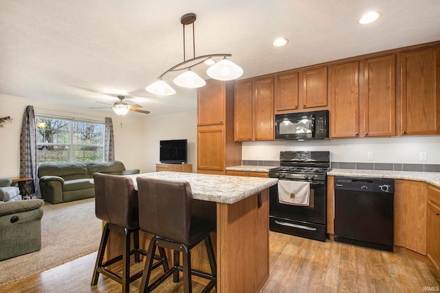 kitchen with light wood-type flooring, a breakfast bar, black appliances, a kitchen island, and hanging light fixtures