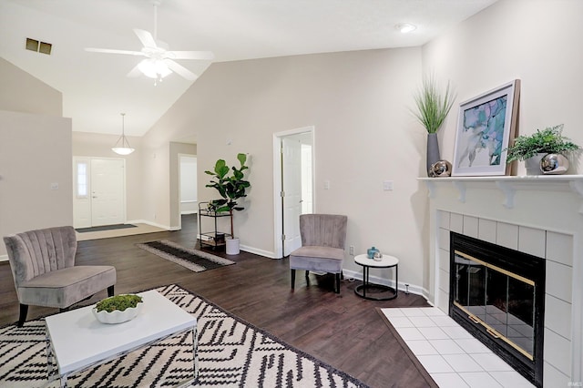 living room with ceiling fan, a tiled fireplace, high vaulted ceiling, and light hardwood / wood-style flooring