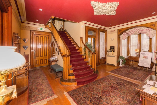 foyer with wood-type flooring, ornamental molding, and an inviting chandelier