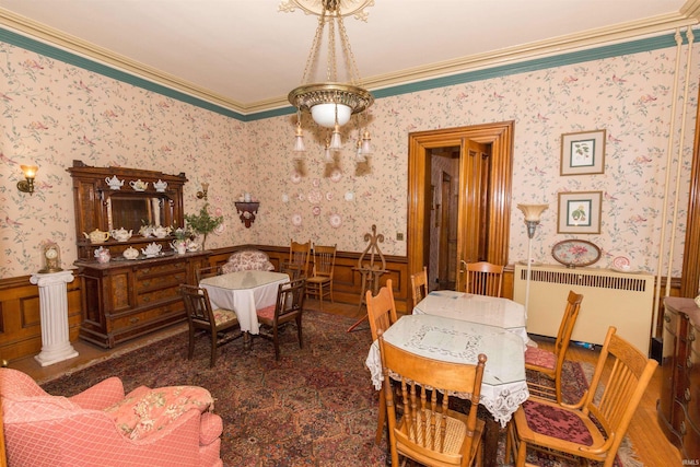 dining space with radiator, crown molding, wooden walls, and a notable chandelier