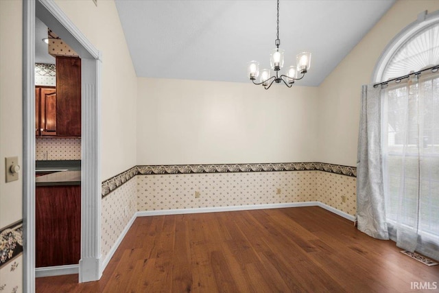 unfurnished dining area with a chandelier, dark wood-type flooring, and vaulted ceiling