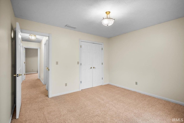 unfurnished bedroom with a closet, light colored carpet, and a textured ceiling