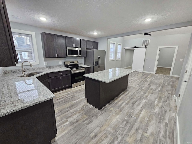 kitchen with a barn door, a center island, a textured ceiling, and appliances with stainless steel finishes