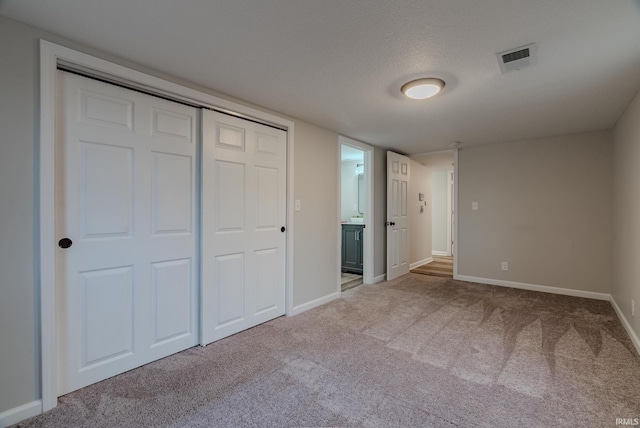 unfurnished bedroom with a textured ceiling, ensuite bathroom, light carpet, and a closet