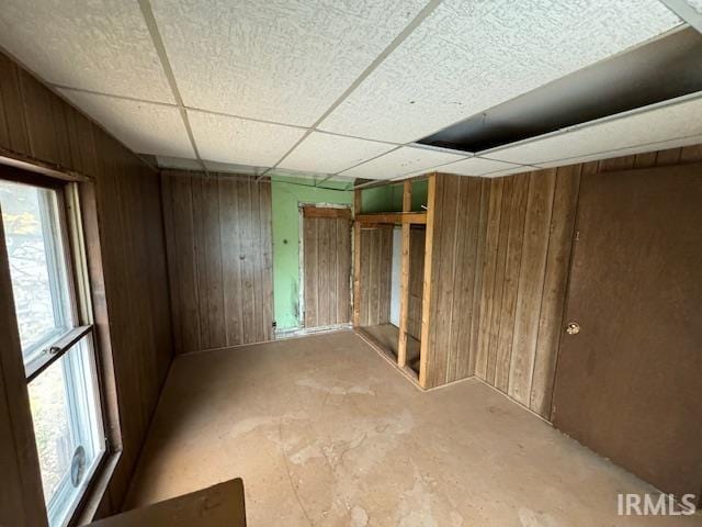 basement featuring a paneled ceiling, wood walls, and plenty of natural light