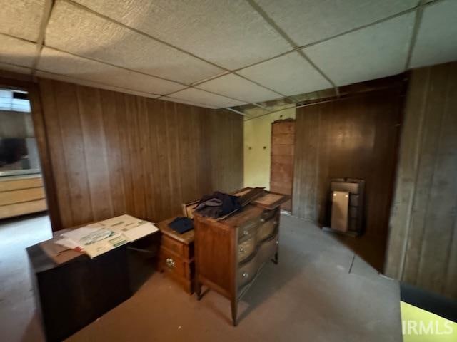 misc room with a paneled ceiling, wood walls, and concrete flooring