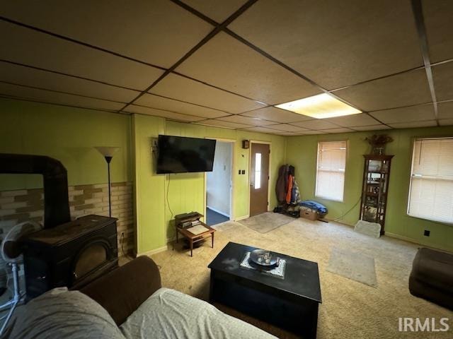 living room featuring a paneled ceiling, a wood stove, and carpet floors