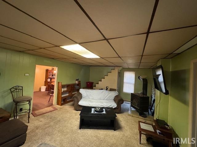 carpeted living room with a drop ceiling and a wood stove