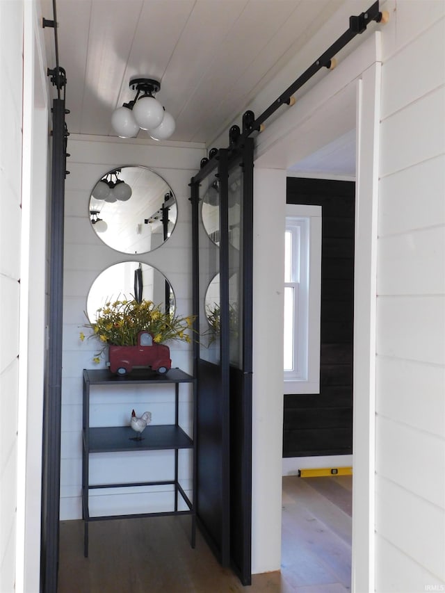 corridor with a barn door, wooden walls, and wood-type flooring