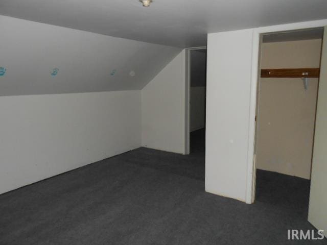 bonus room with dark carpet and vaulted ceiling