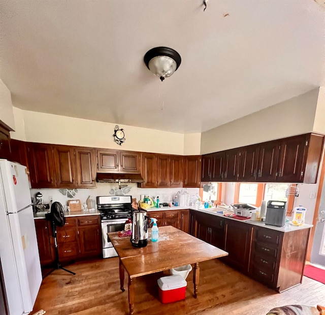 kitchen featuring stainless steel gas stove, freestanding refrigerator, light countertops, light wood-type flooring, and under cabinet range hood