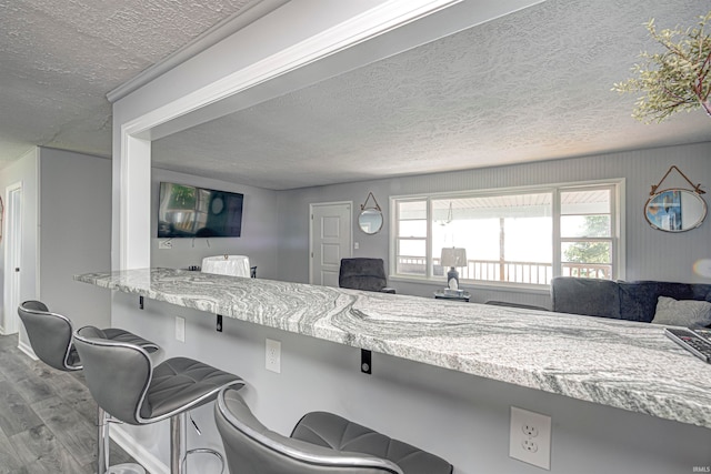 kitchen with a kitchen breakfast bar, light stone countertops, a textured ceiling, and light hardwood / wood-style flooring