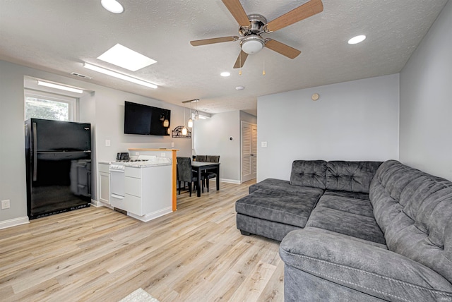 living room with ceiling fan, light hardwood / wood-style floors, and a textured ceiling