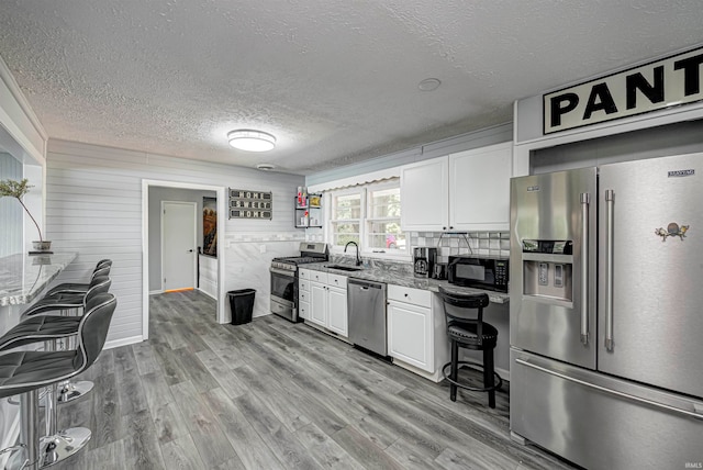 kitchen with decorative backsplash, stainless steel appliances, sink, white cabinets, and light hardwood / wood-style floors