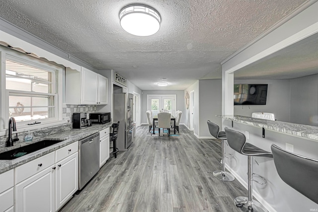 kitchen featuring light stone countertops, white cabinetry, sink, stainless steel dishwasher, and light hardwood / wood-style floors