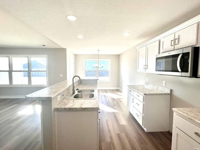 kitchen featuring sink, hardwood / wood-style flooring, an island with sink, white cabinets, and decorative light fixtures