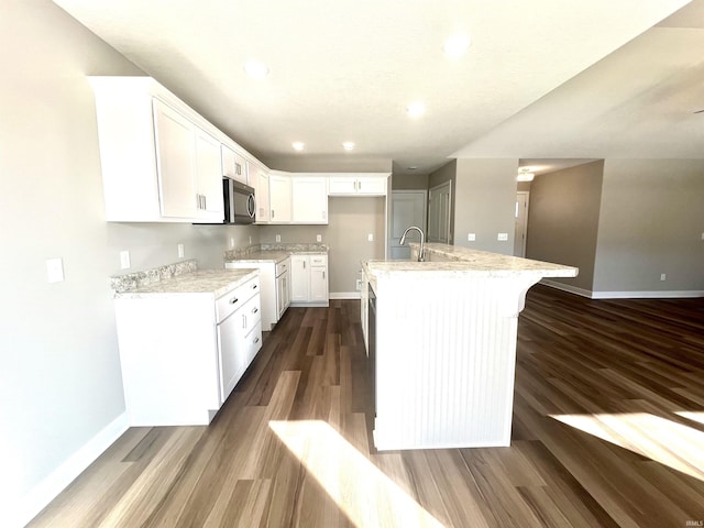 kitchen with dark hardwood / wood-style floors, an island with sink, sink, white cabinets, and light stone countertops