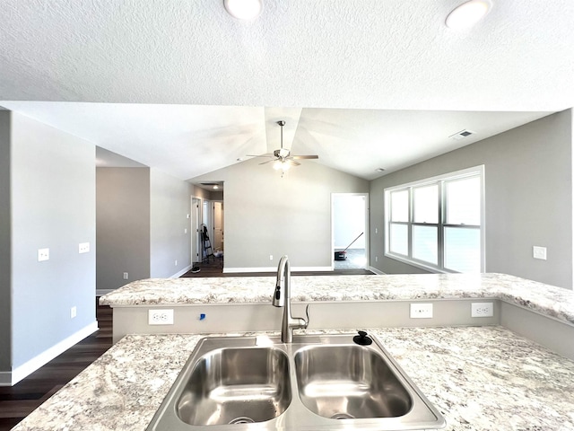 kitchen featuring vaulted ceiling, dark hardwood / wood-style floors, sink, ceiling fan, and light stone countertops