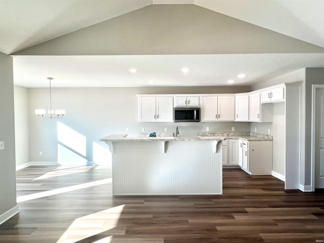 kitchen featuring white cabinetry, light stone counters, decorative light fixtures, dark hardwood / wood-style flooring, and an island with sink