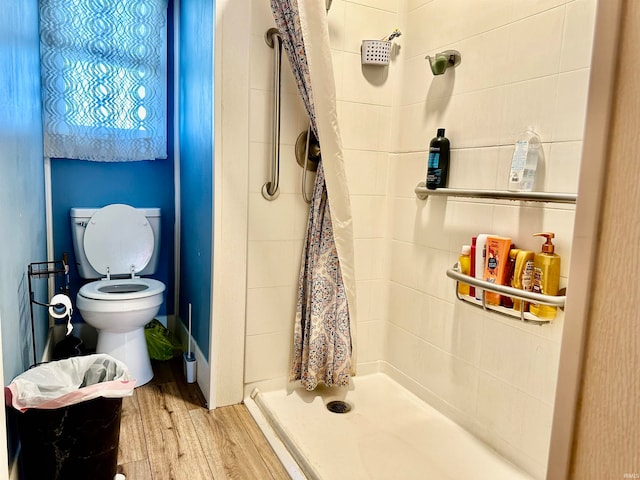 bathroom with tiled shower, wood-type flooring, and toilet