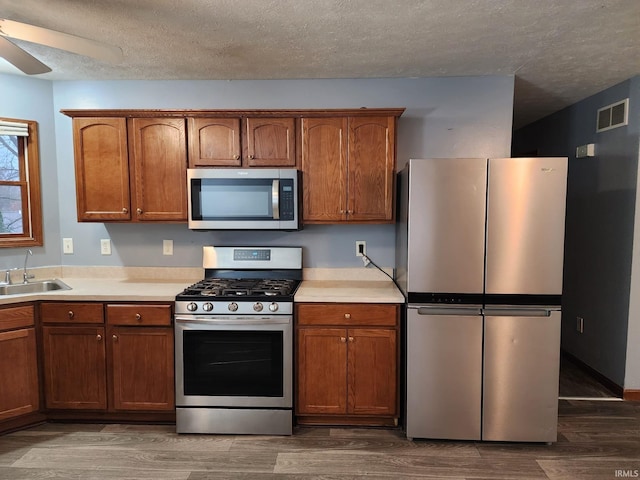 kitchen with sink, ceiling fan, a textured ceiling, dark hardwood / wood-style flooring, and stainless steel appliances