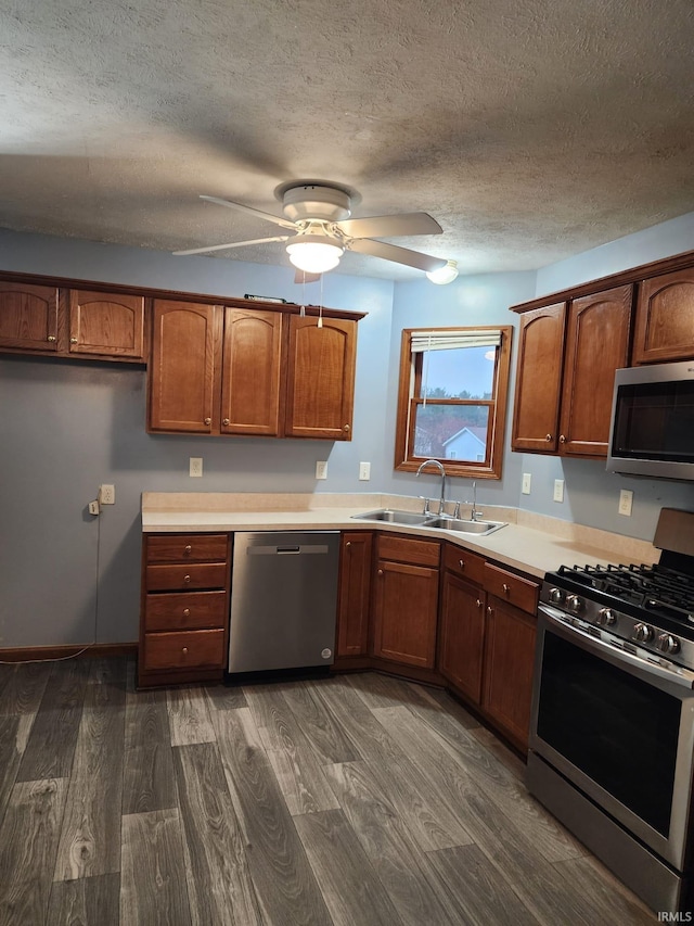 kitchen featuring appliances with stainless steel finishes, a textured ceiling, ceiling fan, sink, and dark hardwood / wood-style floors