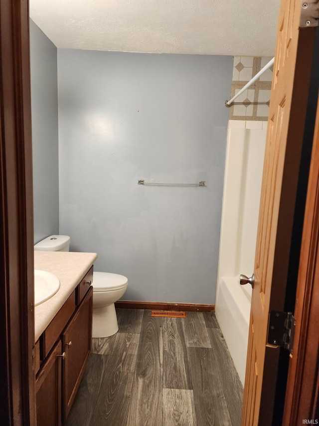 full bathroom featuring vanity, shower / washtub combination, toilet, a textured ceiling, and wood-type flooring