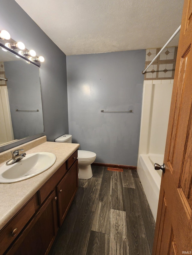 full bathroom with wood-type flooring,  shower combination, a textured ceiling, toilet, and vanity