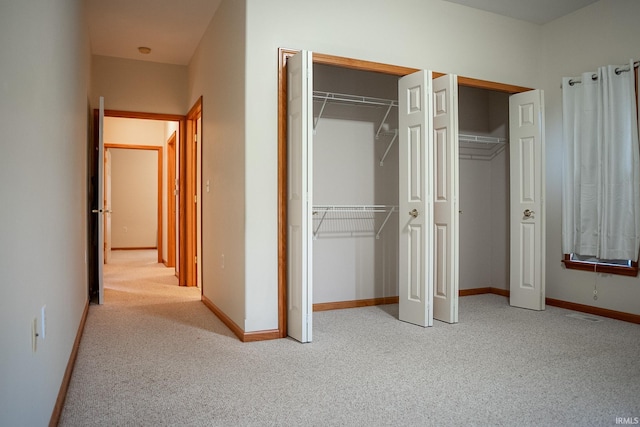 unfurnished bedroom featuring light carpet and multiple closets