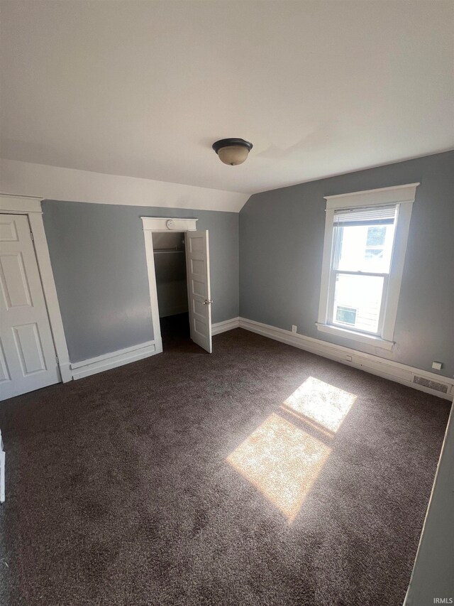 unfurnished bedroom with vaulted ceiling, dark carpet, and a closet