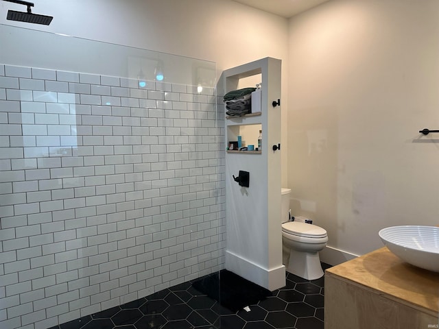 bathroom featuring tile patterned flooring, tiled shower, toilet, and sink