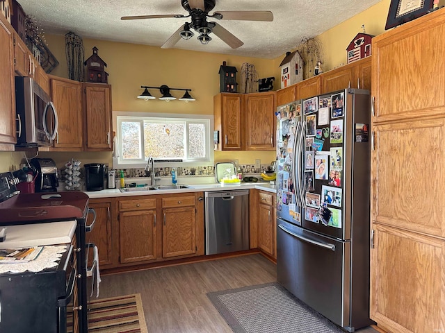 kitchen with appliances with stainless steel finishes, a textured ceiling, dark hardwood / wood-style flooring, and sink