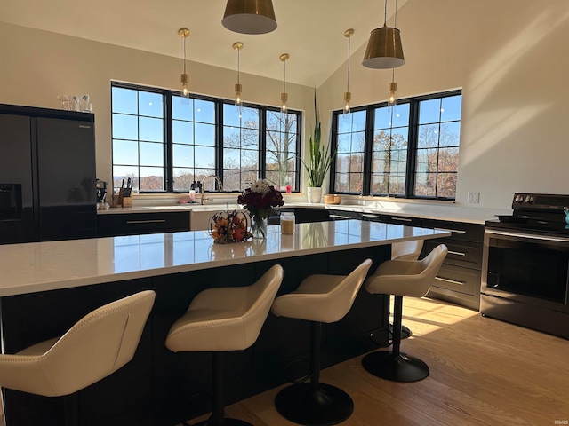 kitchen featuring a kitchen breakfast bar, stainless steel range with electric stovetop, vaulted ceiling, pendant lighting, and light hardwood / wood-style floors