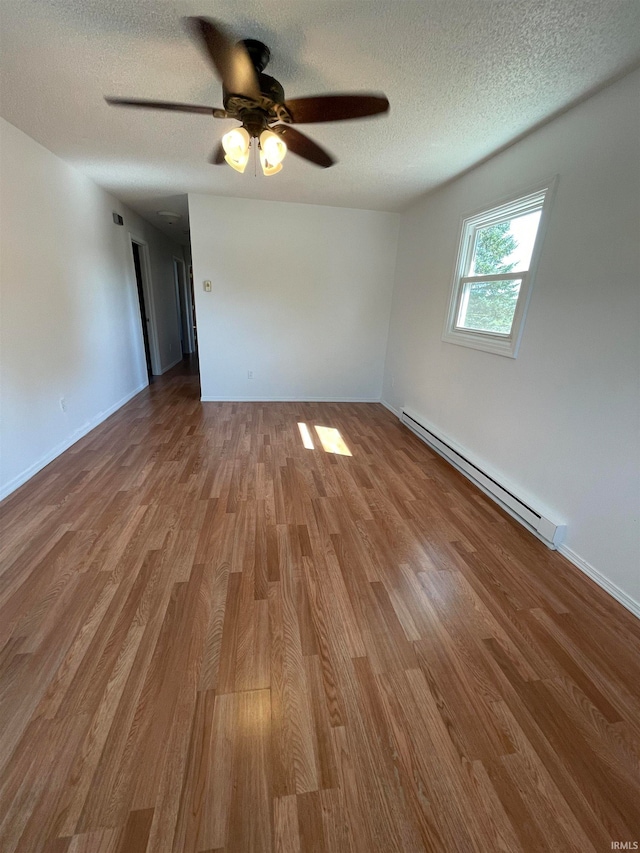 empty room with ceiling fan, hardwood / wood-style floors, a textured ceiling, and a baseboard heating unit