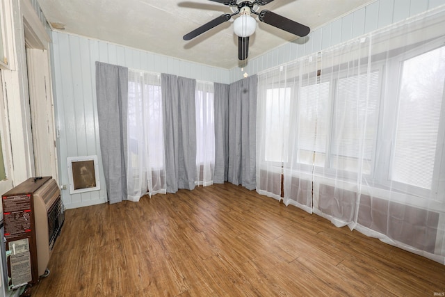 empty room featuring hardwood / wood-style floors, heating unit, ceiling fan, and wooden walls