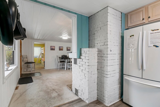 kitchen featuring carpet flooring, light brown cabinetry, white fridge, and brick wall