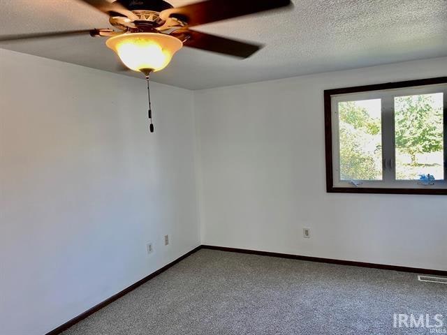 carpeted spare room featuring ceiling fan and a textured ceiling