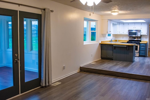 kitchen with white cabinets, appliances with stainless steel finishes, kitchen peninsula, and dark wood-type flooring