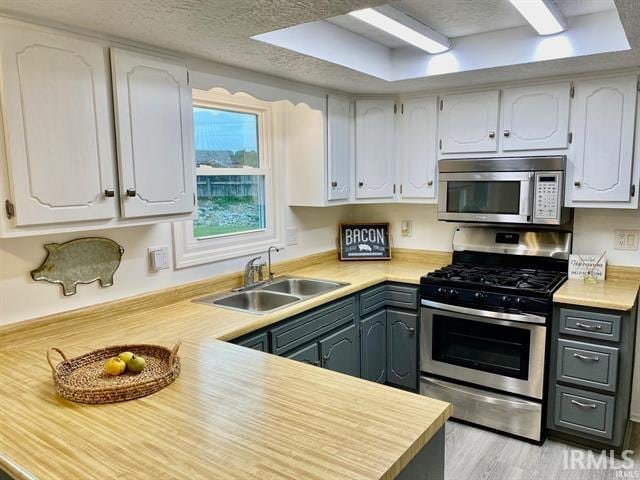 kitchen featuring sink, a textured ceiling, light hardwood / wood-style floors, white cabinetry, and stainless steel appliances