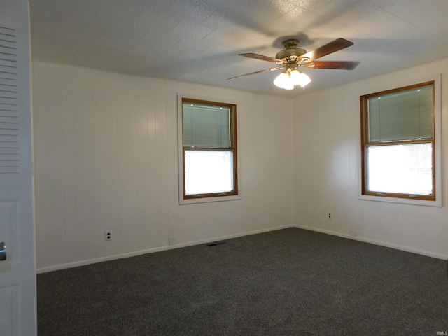 empty room with ceiling fan, a healthy amount of sunlight, and dark carpet