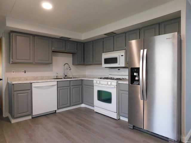 kitchen with gray cabinets, wood-type flooring, white appliances, and sink