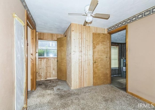 carpeted empty room with water heater, ceiling fan, and wood walls