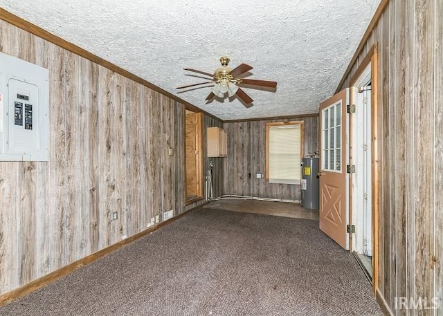 unfurnished room featuring a textured ceiling, ceiling fan, water heater, electric panel, and wood walls