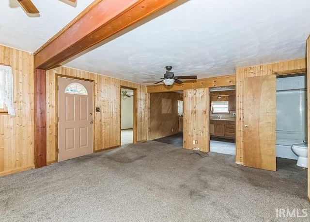 unfurnished living room featuring dark colored carpet, ceiling fan, and wooden walls