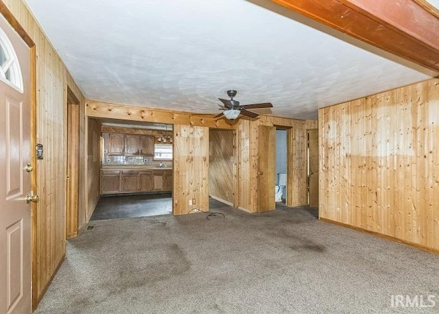 unfurnished living room featuring wood walls and dark carpet